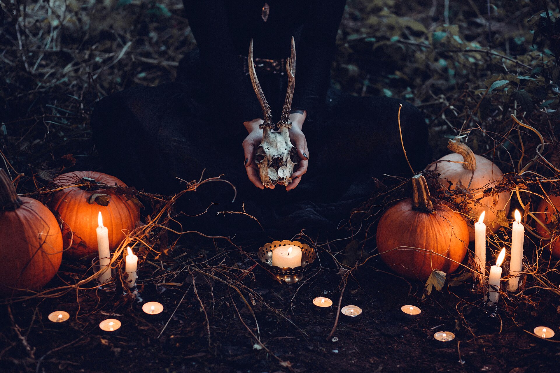 Candles and pumpkins around a skull held in the dark