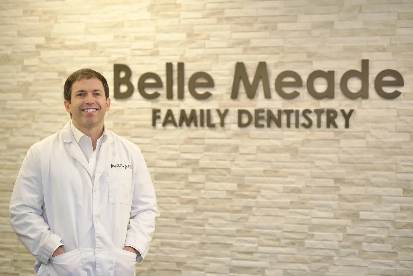 Dr. Pace Jr. in a white coat in front of the 'Belle Meade Family Dentistry' sign wall